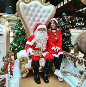 Père Noël et assistante posant devant décor festif.